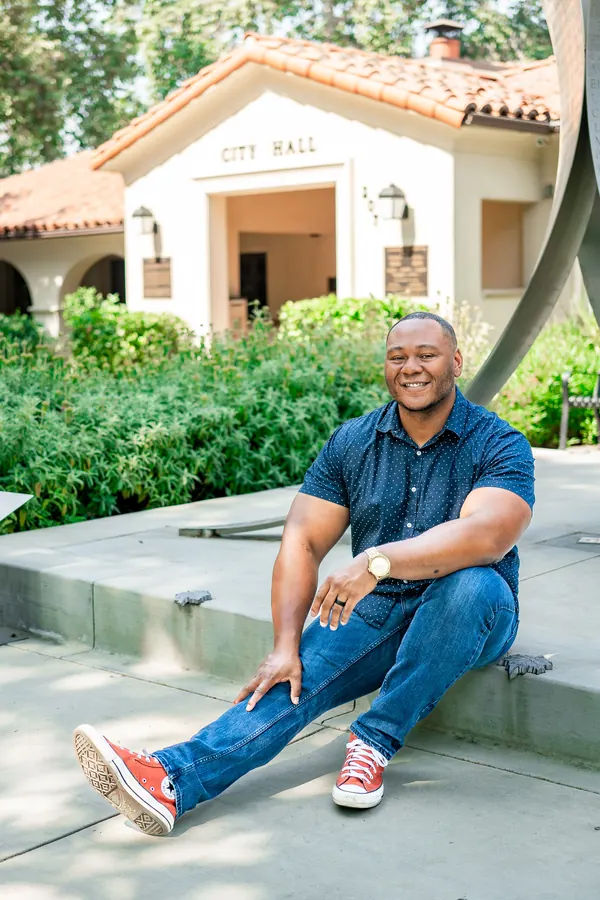 Smiling man seated outside a Spanish-style city hall