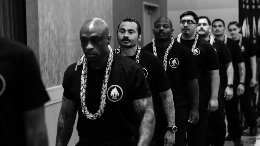 Black-and-white photo of a line of men wearing leis walking in a ceremony