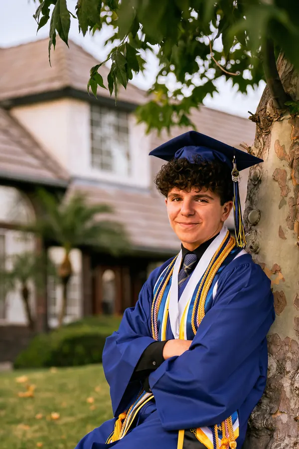 Graduate in a blue gown and stole leaning against a tree