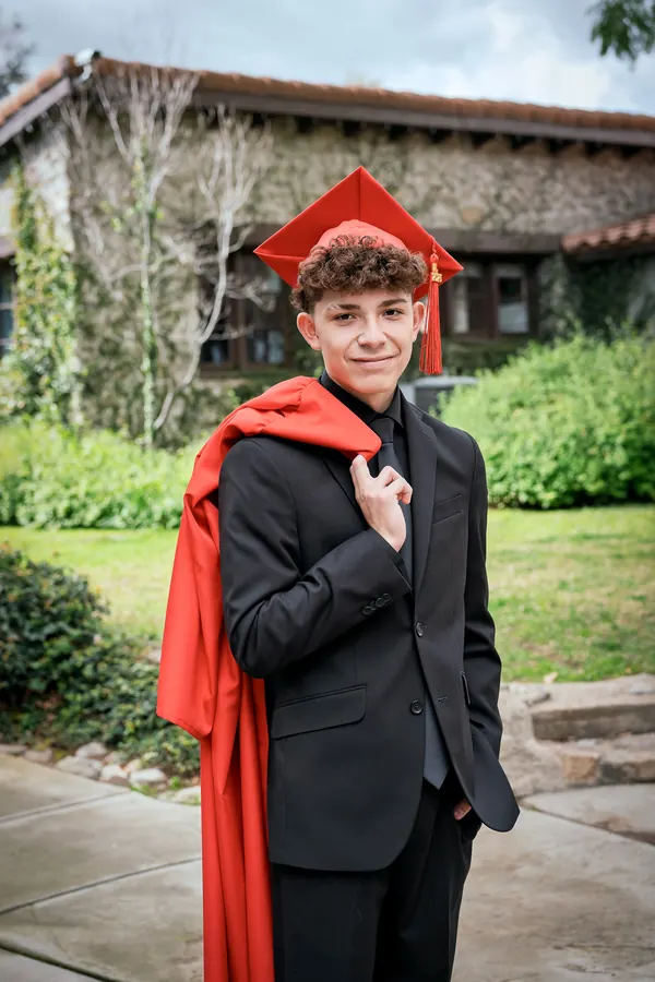 Young graduate in a suit and red cap holding a red gown over his shoulder
