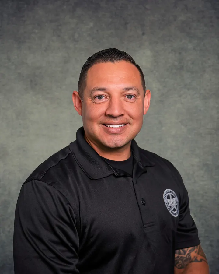 Smiling man in a black logo polo, studio headshot
