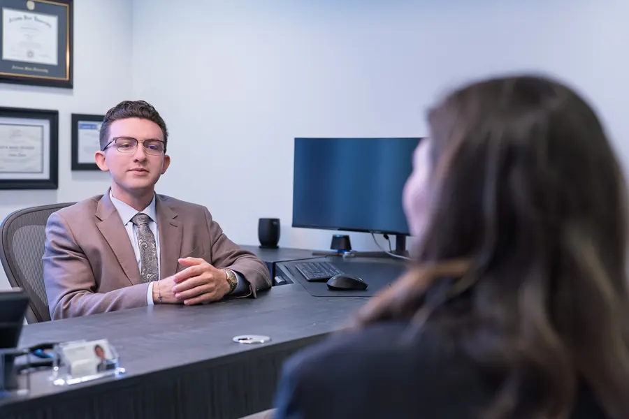 Attorney in a tan suit seated at his desk in conversation with a client