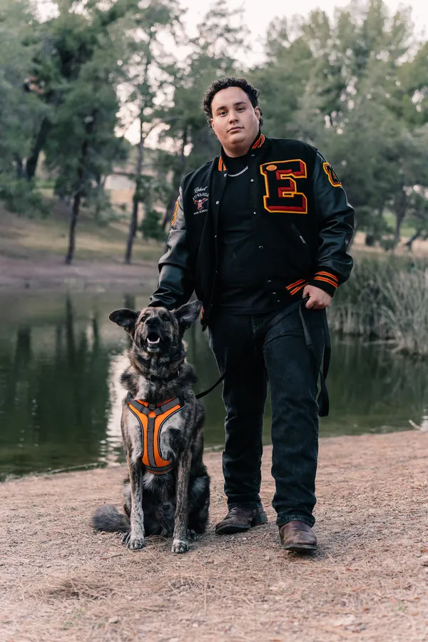 Young man in a letterman jacket with his dog beside a pond