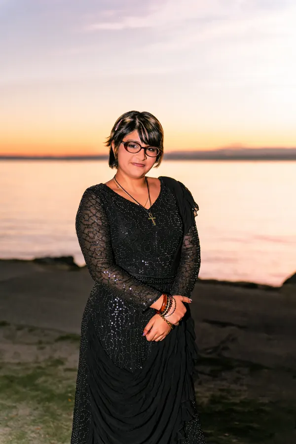 Young woman in a black sequined dress at sunset by the ocean